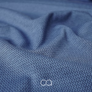 Op de afbeelding: Close-up van een blauwe stof met een textuur, geweven patroon. De stof is zacht en heeft een subtiele glans.