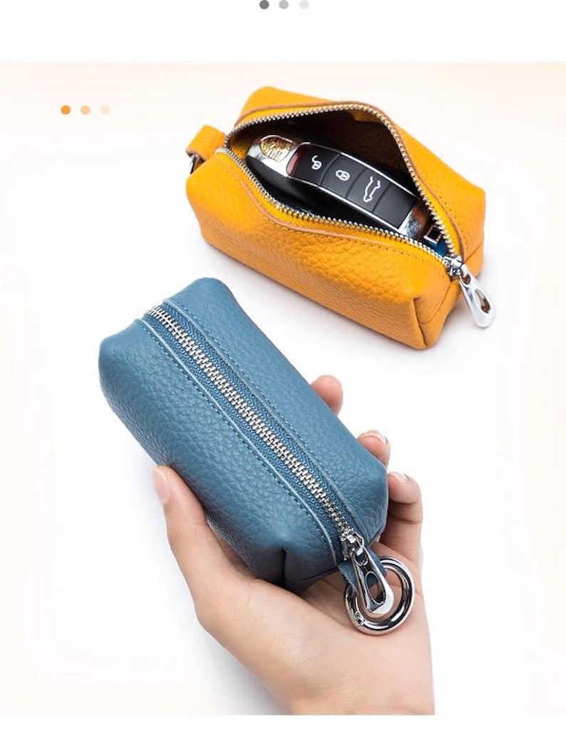 May include: Two leather key cases. One is open, revealing a car key inside, and is a bright yellow-orange color. The other is a blue-grey color and is closed, with a silver zipper and a silver clasp.