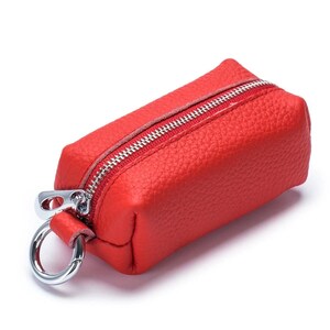 May include: A small, rectangular red leather key case with a silver zipper and a silver metal ring. The key case has a textured surface and a simple, minimalist design.