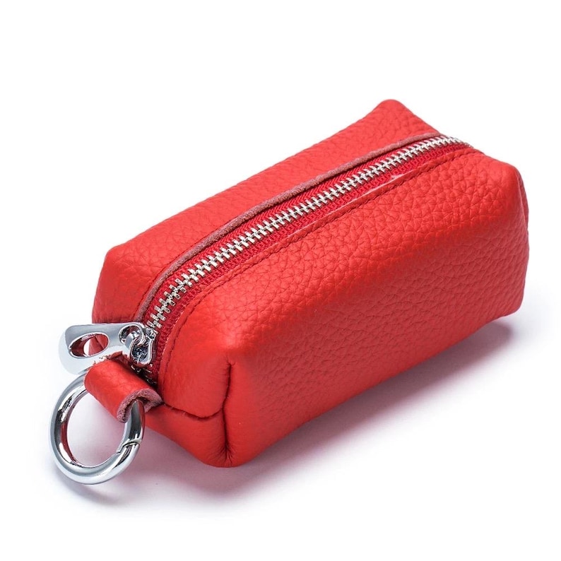 May include: A small, rectangular red leather key case with a silver zipper and a silver metal ring. The key case has a textured surface and a simple, minimalist design.