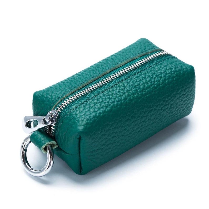 May include: A small, emerald green leather key case with a silver zipper and a silver key ring. The key case has a textured surface and a rectangular shape. The zipper runs along the top of the case.