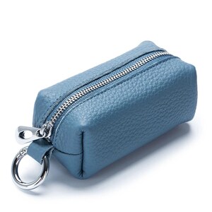 May include: A blue leather key case with a silver zipper and a silver key ring. The rectangular case has a textured surface and a small loop for the key ring. The zipper runs along the top of the case.