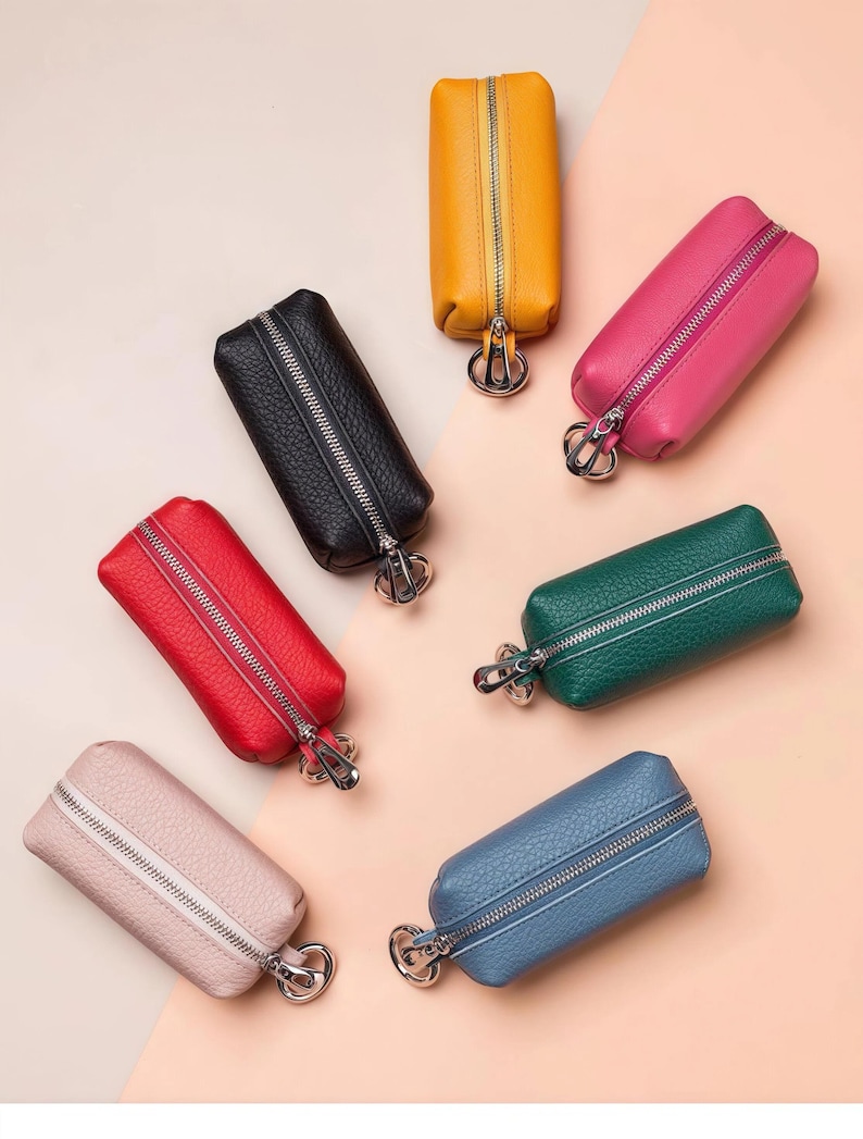 May include: An assortment of colorful key cases in various shades, including yellow, pink, green, blue, red, black, and light pink. Each case is rectangular with a zipper closure and a silver-toned key ring attachment. The cases are made of a textured material.