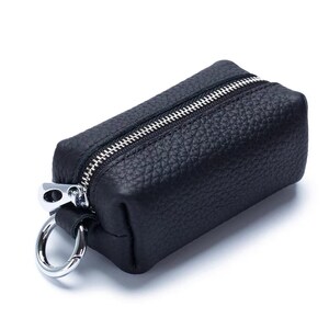 May include: A small, rectangular black leather key case with a silver zipper and a silver key ring. The leather has a textured appearance. The key case is closed and ready for use.