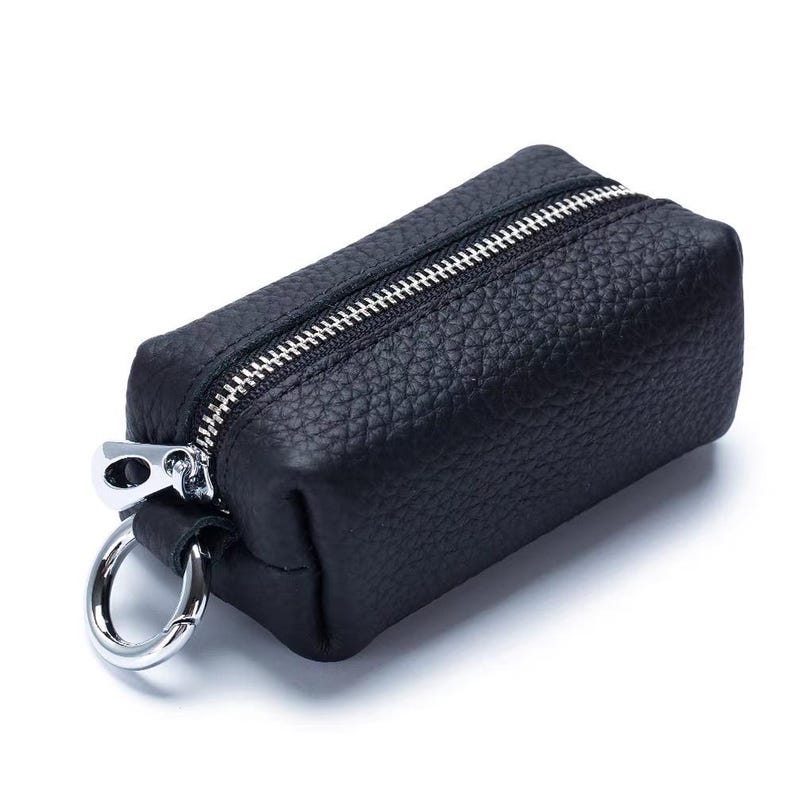 May include: A small, rectangular black leather key case with a silver zipper and a silver key ring. The leather has a textured appearance. The key case is closed and ready for use.
