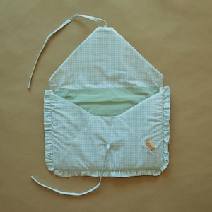 May include: A light green and white gingham fabric envelope-style pouch with a ruffled edge trim. The pouch features a pointed flap, a solid light green interior lining, and two thin fabric ties for closure. A small tan label is attached to the side.