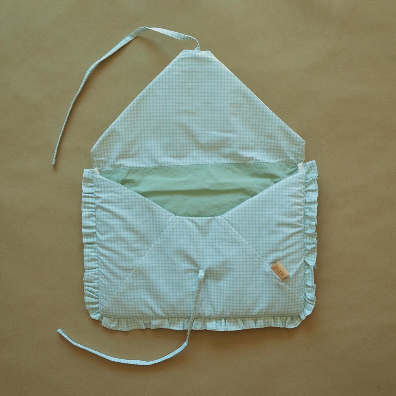 May include: A light green and white gingham fabric envelope-style pouch with a ruffled edge trim. The pouch features a pointed flap, a solid light green interior lining, and two thin fabric ties for closure. A small tan label is attached to the side.