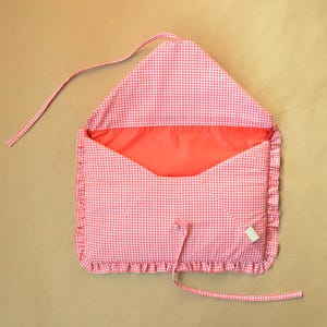 May include: A fabric envelope-style pouch featuring a red and white gingham check pattern. The pouch has a ruffled border, a solid red interior lining, and two long fabric ties attached to the top flap and the bottom edge for closure.