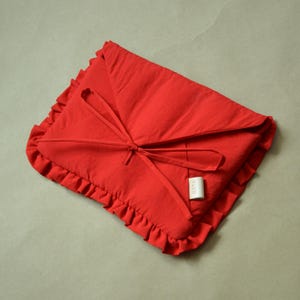May include: A bright red, envelope-style pillow cover with a ruffled edge and a matching tie closure. The pillow cover is made of a soft fabric and has a small, rectangular tag attached to the side.