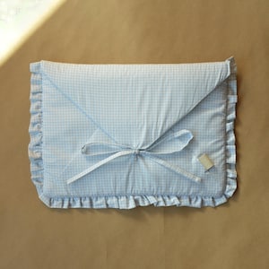 May include: A rectangular fabric envelope case featuring a light blue and white gingham check pattern. The case has a triangular flap closure secured with thin fabric ties and is finished with a ruffled border along the edges. A small tag is attached.