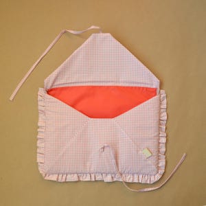 May include: A fabric envelope-style pouch featuring a light pink and white gingham pattern. The exterior is trimmed with a ruffled edge, and the interior is lined with a solid coral-colored fabric. Two thin fabric ties are attached for closure.
