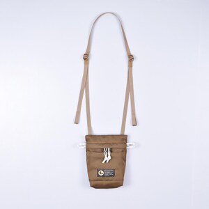 May include: A brown canvas pouch with a drawstring closure and a small front pocket. The pouch has a tan adjustable strap and a white logo that says "Flylow Gear".