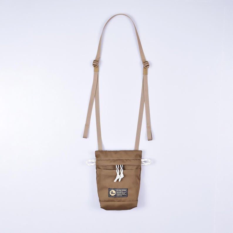 May include: A brown canvas pouch with a drawstring closure and a small front pocket. The pouch has a tan adjustable strap and a white logo that says "Flylow Gear".