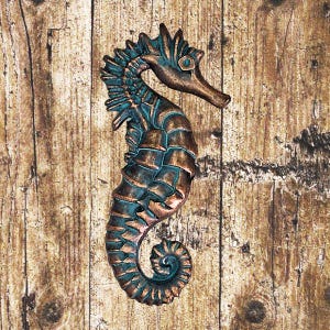 May include: A blue and copper colored seahorse wall decor. The seahorse is made of metal and has a detailed design.