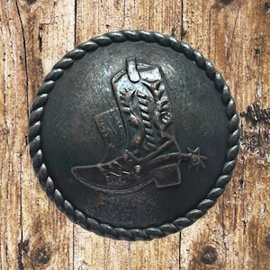 Peut inclure: Un bouton rond en métal brun foncé avec un motif en relief d'une botte de cowboy avec une éperon. Le bouton a une bordure en forme de corde.