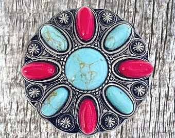 May include: A silver and turquoise jewelry buckle with a circular design. The buckle features eight turquoise stones and eight red stones set in a silver frame.