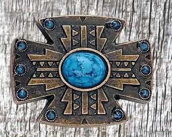 May include: A bronze cross-shaped decorative piece with a turquoise-colored stone in the center. The cross has a geometric design with triangles and a distressed finish.