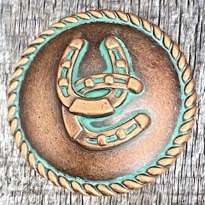 Pode incluir: Uma fivela de cinto de cobre com uma borda de corda e duas ferraduras turquesa no centro.