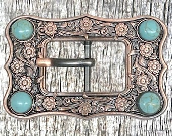May include: Ornate copper-toned belt buckle with turquoise-colored stone accents. The rectangular buckle features floral and scrollwork designs, with four round turquoise stones. The buckle has a classic pin and frame closure.