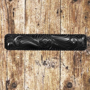 May include: Black leather belt buckle with a detailed floral design. The buckle is rectangular and has a rope-like border.