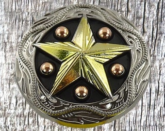 May include: A silver and gold belt buckle with a five-pointed star design. The star is raised and has a black background. The buckle is surrounded by a decorative border.