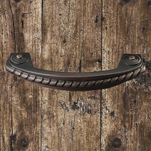 Peut inclure: Une poignée de porte en métal noir avec un motif de corde et une forme légèrement incurvée. La poignée a une finition brossée et deux boutons ronds aux extrémités.