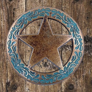 Op de afbeelding: Een rustiek, rond, metalen wanddecor met een vijfpuntige ster en een turquoiseblauw bloemmotief rondom de omtrek.