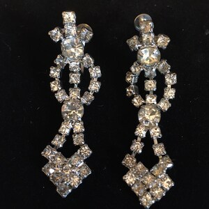 Puede incluir: Un par de pendientes colgantes de plata con detalles de pedrer&iacute;a transparente. Los pendientes tienen forma de l&aacute;grima con un racimo de pedrer&iacute;a en la parte superior y un dise&ntilde;o en cascada de pedrer&iacute;a m&aacute;s peque&ntilde;a.