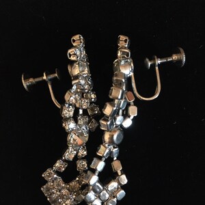 Puede incluir: Un par de pendientes de clip plateados con un dise&ntilde;o colgante que presenta m&uacute;ltiples filas de diamantes de imitaci&oacute;n transparentes.