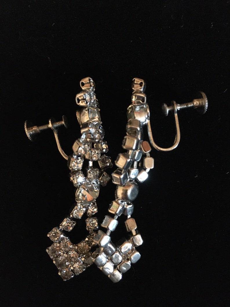 Puede incluir: Un par de pendientes de clip plateados con un dise&ntilde;o colgante que presenta m&uacute;ltiples filas de diamantes de imitaci&oacute;n transparentes.