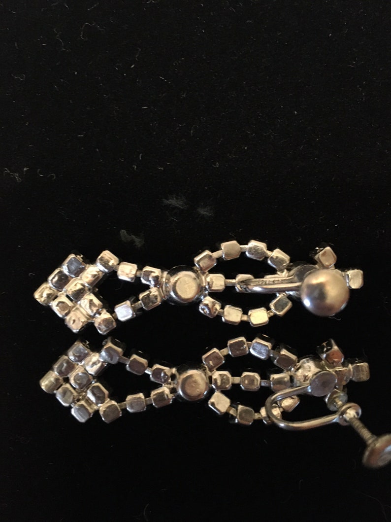 Puede incluir: Un par de pendientes de clip de tono plateado con un dise&ntilde;o de l&aacute;grima. Los pendientes est&aacute;n hechos de varias filas de peque&ntilde;os diamantes de imitaci&oacute;n transparentes.