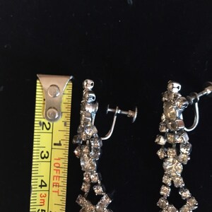 Puede incluir: Un par de pendientes de clip plateados con un dise&ntilde;o de l&aacute;grima. Los pendientes est&aacute;n adornados con diamantes de imitaci&oacute;n transparentes.