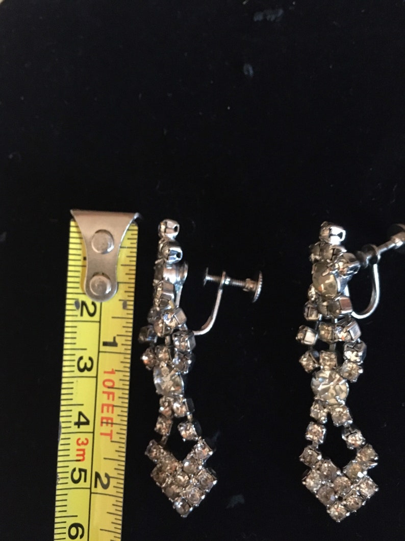 Puede incluir: Un par de pendientes de clip plateados con un dise&ntilde;o de l&aacute;grima. Los pendientes est&aacute;n adornados con diamantes de imitaci&oacute;n transparentes.