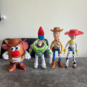 May include: Four Toy Story character figures: Mr. Potato Head, Buzz Lightyear, Woody, and Jessie. Mr. Potato Head wears a brown cowboy hat. Buzz Lightyear has a rocket on his back. Woody and Jessie wear cowboy hats and boots.