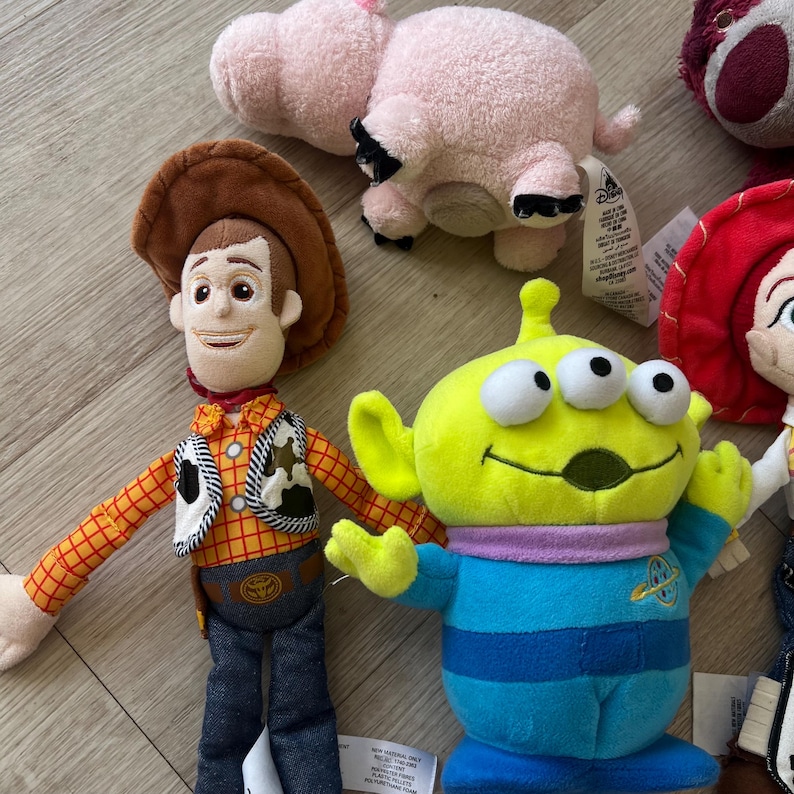 K&ouml;nnte beinhalten: Eine Sammlung von Pl&uuml;schtieren mit Charakteren aus dem Animationsfilm Toy Story. Die Spielzeuge umfassen Woody, einen Alien mit drei Augen, ein rosa Schwein und Jessie. Die Spielzeuge sind aus weichen Materialien gefertigt und weisen detaillierte Merkmale auf.