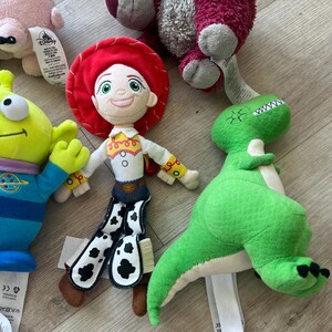 K&ouml;nnte beinhalten: Eine Sammlung von Pl&uuml;schtieren mit Charakteren aus dem Toy Story-Franchise. Die Spielzeuge umfassen Jessie, einen gr&uuml;nen Dinosaurier und einen dreiaugigen Au&szlig;erirdischen. Die Spielzeuge sind aus weichen Materialien gefertigt und haben detaillierte Gesichtsz&uuml;ge.