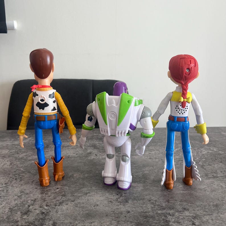 K&ouml;nnte beinhalten: Drei Kunststoff-Actionfiguren von Charakteren aus dem Animationsfilm Toy Story. Woody, in Cowboy-Kleidung, Buzz Lightyear, ein Weltraumranger, und Jessie, ein Cowgirl, stehen nebeneinander. Die Figuren sind farbenfroh und detailliert.