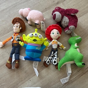 K&ouml;nnte beinhalten: Eine Sammlung von Pl&uuml;schtieren mit Charakteren aus dem Animationsfilm Toy Story. Die Spielzeuge umfassen Woody, Buzz Lightyear, Jessie, Rex, Hamm und Lotso. Jedes Spielzeug hat ein einzigartiges Design und Farbschema mit angebrachten Etiketten.