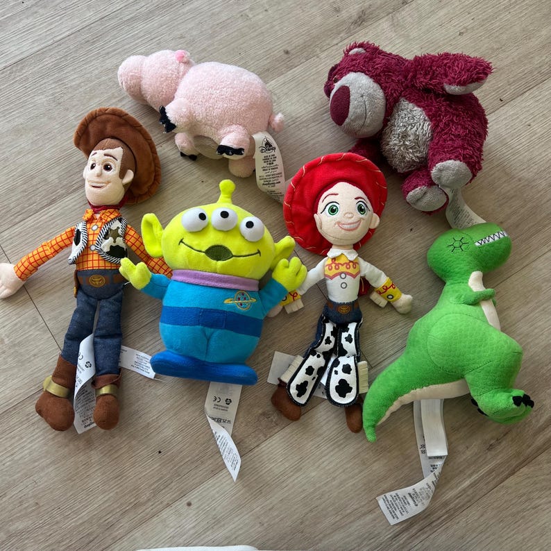 K&ouml;nnte beinhalten: Eine Sammlung von Pl&uuml;schtieren mit Charakteren aus dem Animationsfilm Toy Story. Die Spielzeuge umfassen Woody, Buzz Lightyear, Jessie, Rex, Hamm und Lotso. Jedes Spielzeug hat ein einzigartiges Design und Farbschema mit angebrachten Etiketten.