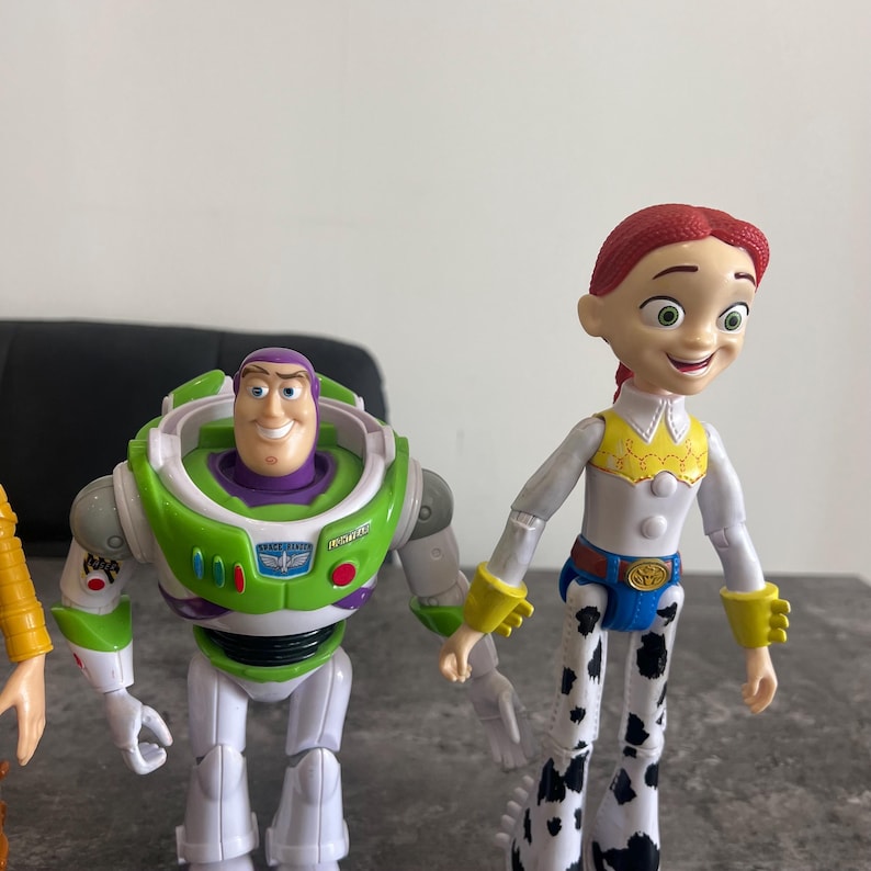 K&ouml;nnte beinhalten: Toy Story-Charakterfiguren von Buzz Lightyear und Jessie. Buzz Lightyear tr&auml;gt einen gr&uuml;nen und wei&szlig;en Raumanzug. Jessie tr&auml;gt ein wei&szlig;es Hemd, blaue Jeans und eine gelbe Weste. Die Figuren sind aus Kunststoff.