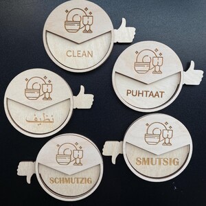 May include: Five wooden round signs with thumbs up and down indicators. The signs have different words and symbols indicating clean or dirty dishes. The words are "Clean", "Puhtaat", "Nظيف", "Schmutzig", and "Smutsig".