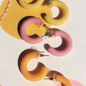 Peut inclure: Un ensemble de quatre boucles d'oreilles créoles en deux couleurs : jaune et rose. Les boucles d'oreilles sont en matériau lisse et mat et ont un design simple et moderne.