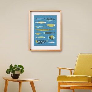 May include: A framed print of a blue background with a pattern of colorful fish in various shapes and sizes. The fish are in shades of blue, yellow, and white.