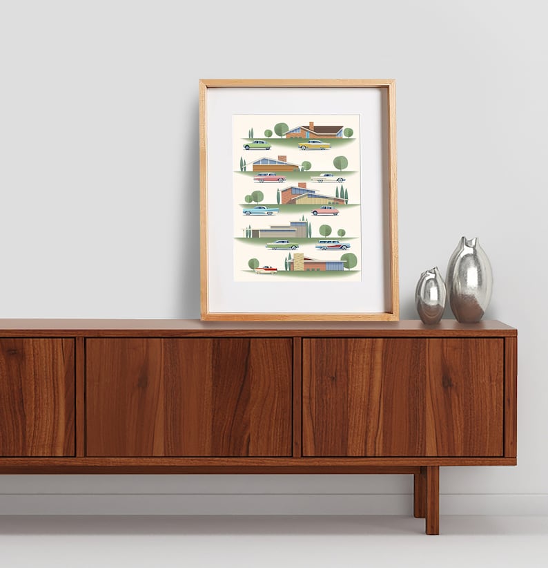 May include: A framed print of a mid-century modern illustration featuring colorful houses and cars. The houses are in various styles and colors, and the cars are all classic models. The print is set against a white background.