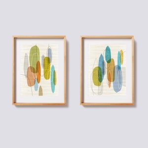 K&ouml;nnte beinhalten: Zwei gerahmte abstrakte Kunstdrucke im Stil der Mid-Century Modern. Die Drucke zeigen &uuml;berlappende geometrische Formen in Blaut&ouml;nen, Gr&uuml;n, Gelb und Orange auf wei&szlig;em Hintergrund.