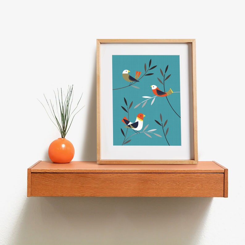 May include: A framed print with a teal background featuring three stylised birds with orange, red, white and black accents perched on branches with grey and green leaves.