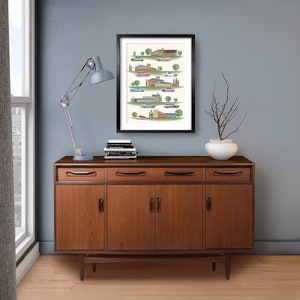 May include: A framed print of a colorful illustration depicting a row of mid-century modern houses with cars parked in front of them. The print is hanging on a light blue wall above a wooden dresser with three drawers and two cabinet doors.