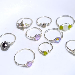 Puede incluir: Una colección de ocho anillos de plata con varias piedras y cuentas de colores. Los anillos presentan una variedad de estilos, incluyendo un anillo con una piedra negra y blanca, un anillo con una piedra morada, un anillo con una piedra verde y un anillo con una piedra blanca.