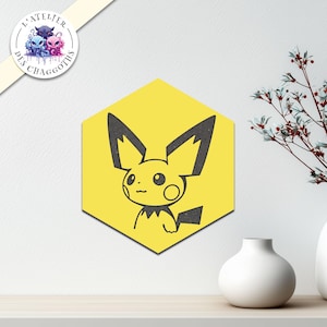 Peut inclure: Une œuvre d'art murale jaune en forme d'hexagone représentant un Pikachu noir. L'œuvre est affichée sur un mur blanc, avec un petit vase blanc et une branche décorative en arrière-plan.