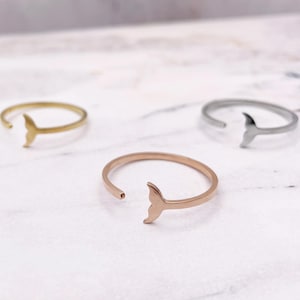 May include: Three adjustable rings with a whale tail design. The rings are gold, rose gold, and silver.